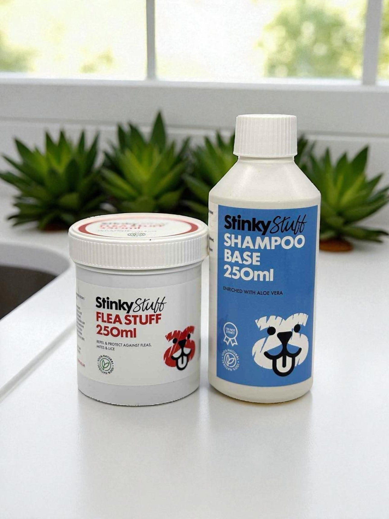 Two bottles of Stinky Stuff pet care products on a surface with plants in the background.